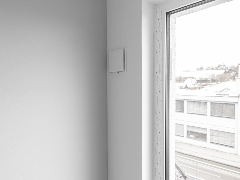 Lüftungsgerät an der Wand neben einem Fenster